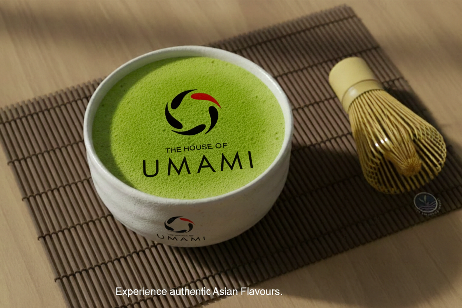Bowl of matcha green tea powder with a whisk on a mat, featuring the House of Umami branding.